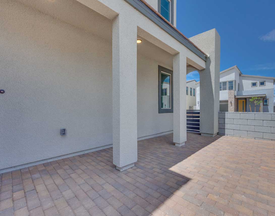 A modern, two-story residential building with a paved entryway and a clear blue sky in the background.