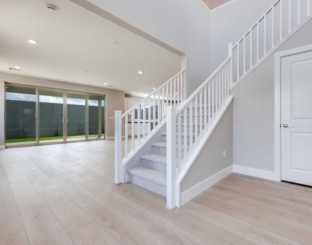 A spacious, open-concept interior with a white staircase leading up to a second level, surrounded by large windows that allow natural light to flood the room.