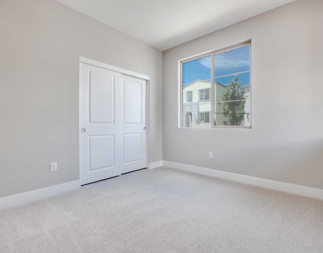 A bright, empty room with a white door and a large window overlooking a residential neighborhood.