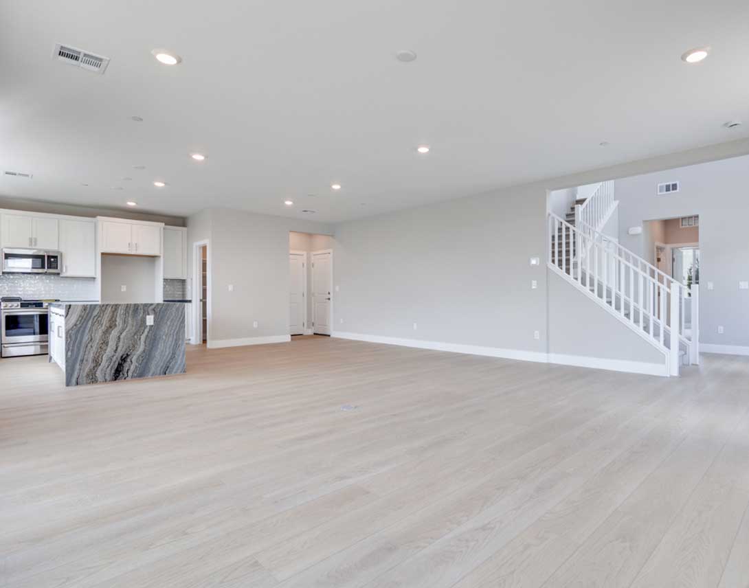 A spacious, open-concept living area with a modern kitchen, hardwood floors, and a staircase leading to an upper level.
