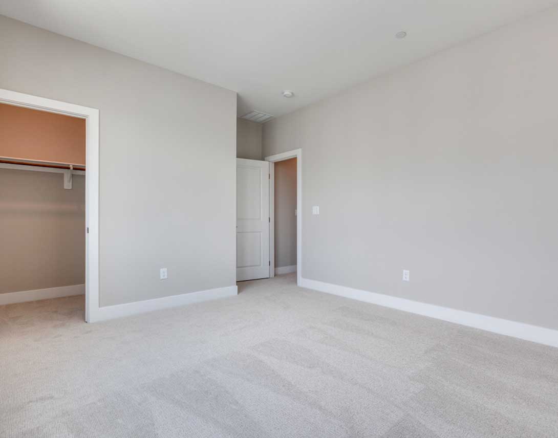 An empty bedroom with white walls, a closet, and a hardwood floor covered in a light-colored carpet.