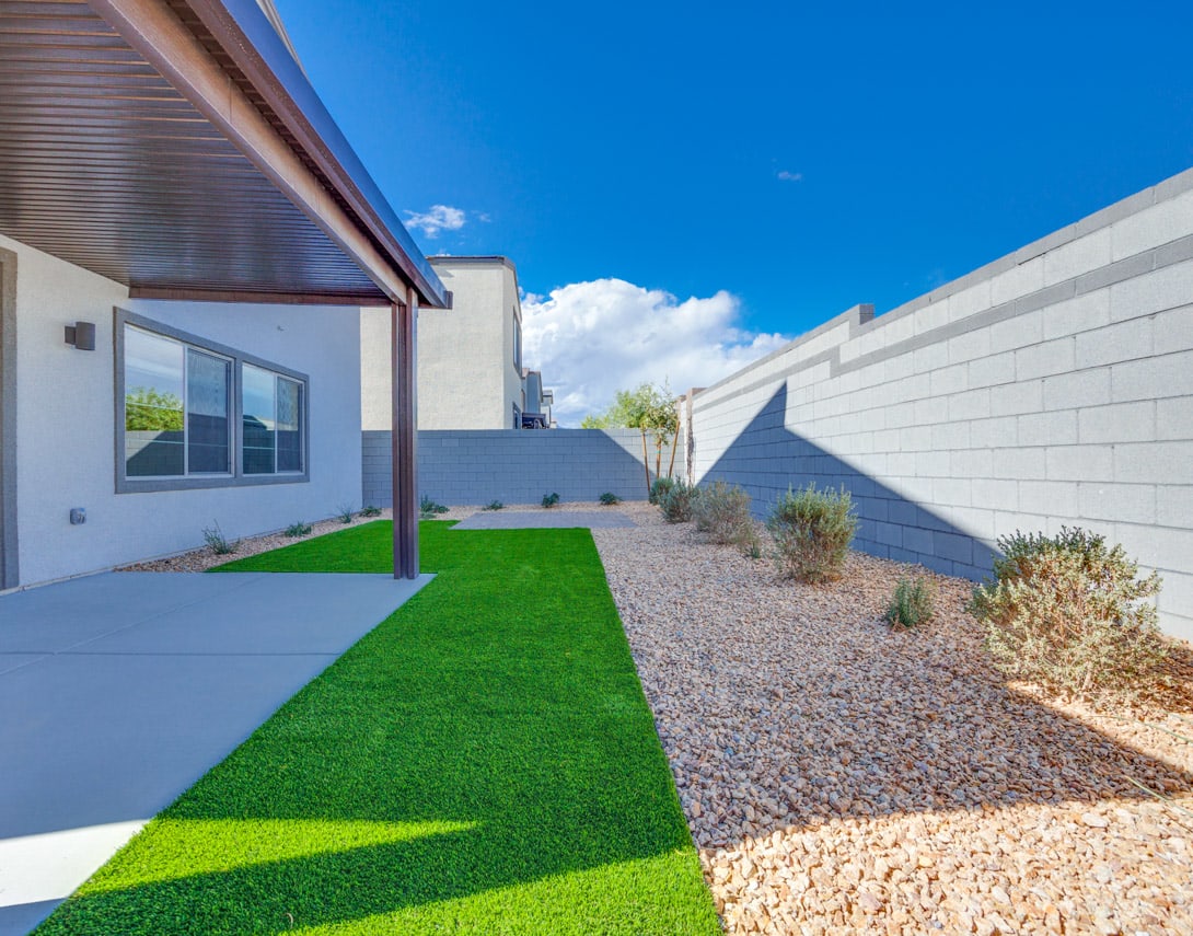 A modern, minimalist exterior with a well-manicured lawn, gravel pathway, and desert-inspired landscaping against a clear blue sky.