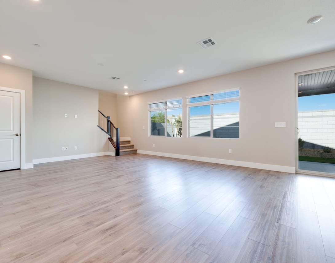 A spacious, open-concept living room with hardwood floors, recessed lighting, and large windows providing natural light.
