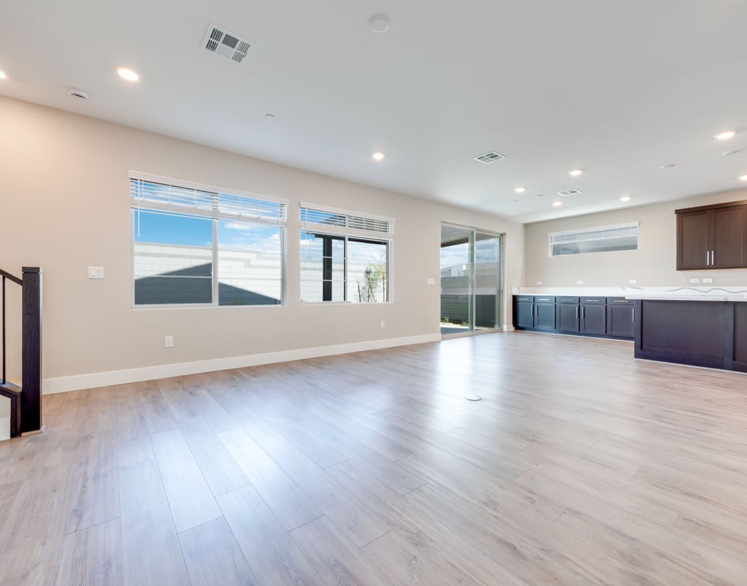 A spacious, open-concept living area with large windows, hardwood floors, and dark cabinetry in the background.