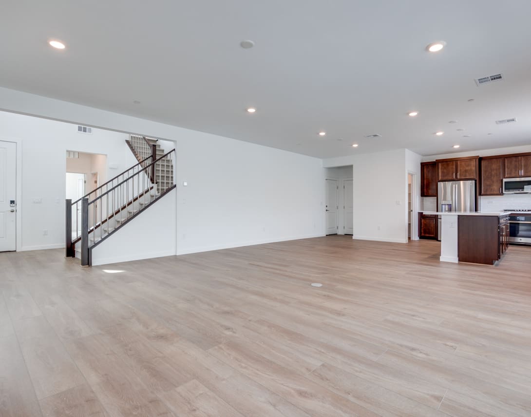A spacious, open-concept living area with hardwood floors, a staircase, and a kitchen visible in the background.