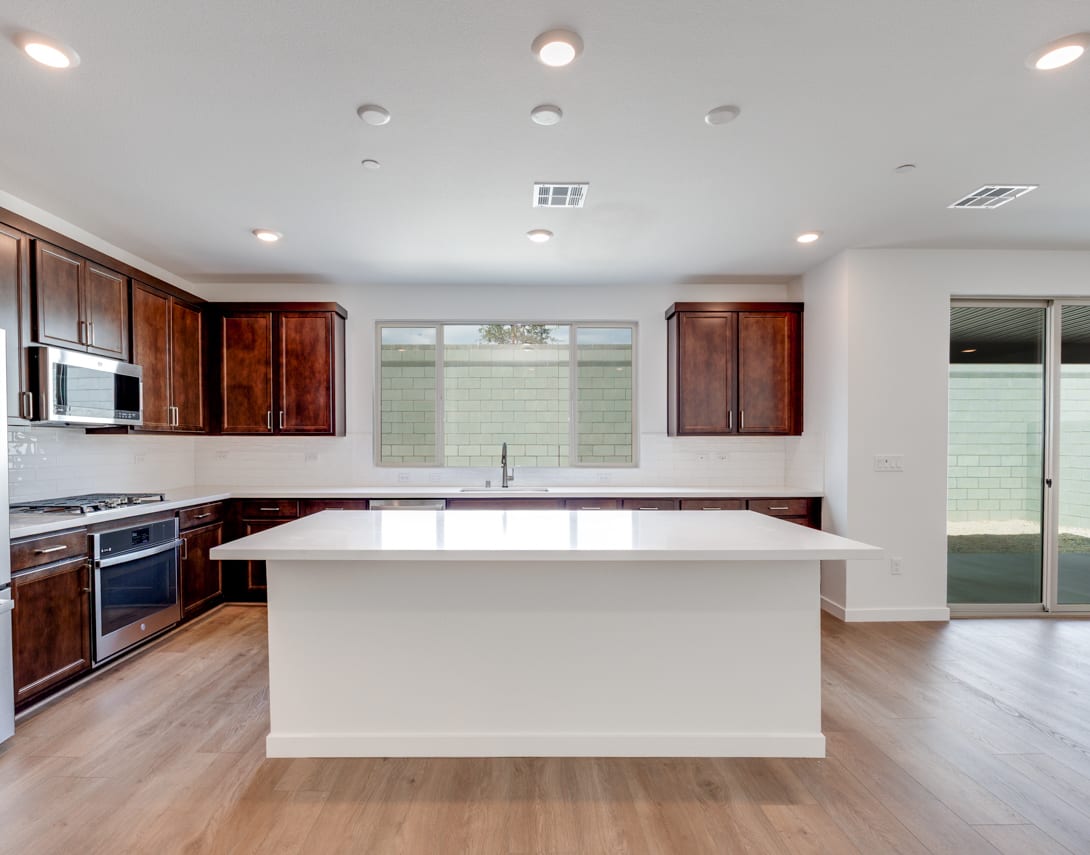 A modern, open-concept kitchen with white countertops, dark wood cabinets, and stainless steel appliances, set against a bright and airy background.