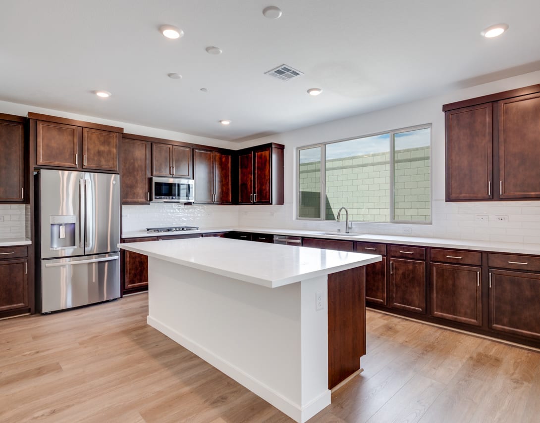 A modern, spacious kitchen with dark wood cabinets, a white countertop island, and stainless steel appliances, set against a bright and airy background.