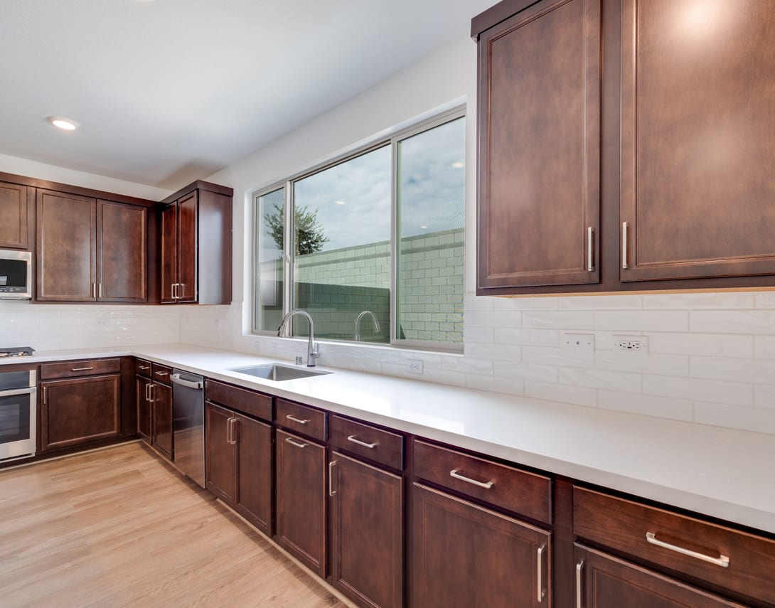 A modern kitchen with dark wood cabinets, a large window, and a white countertop.