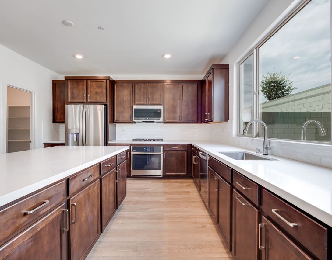 A modern, well-equipped kitchen with dark wood cabinets, stainless steel appliances, and a large window providing natural light and a view of the exterior.