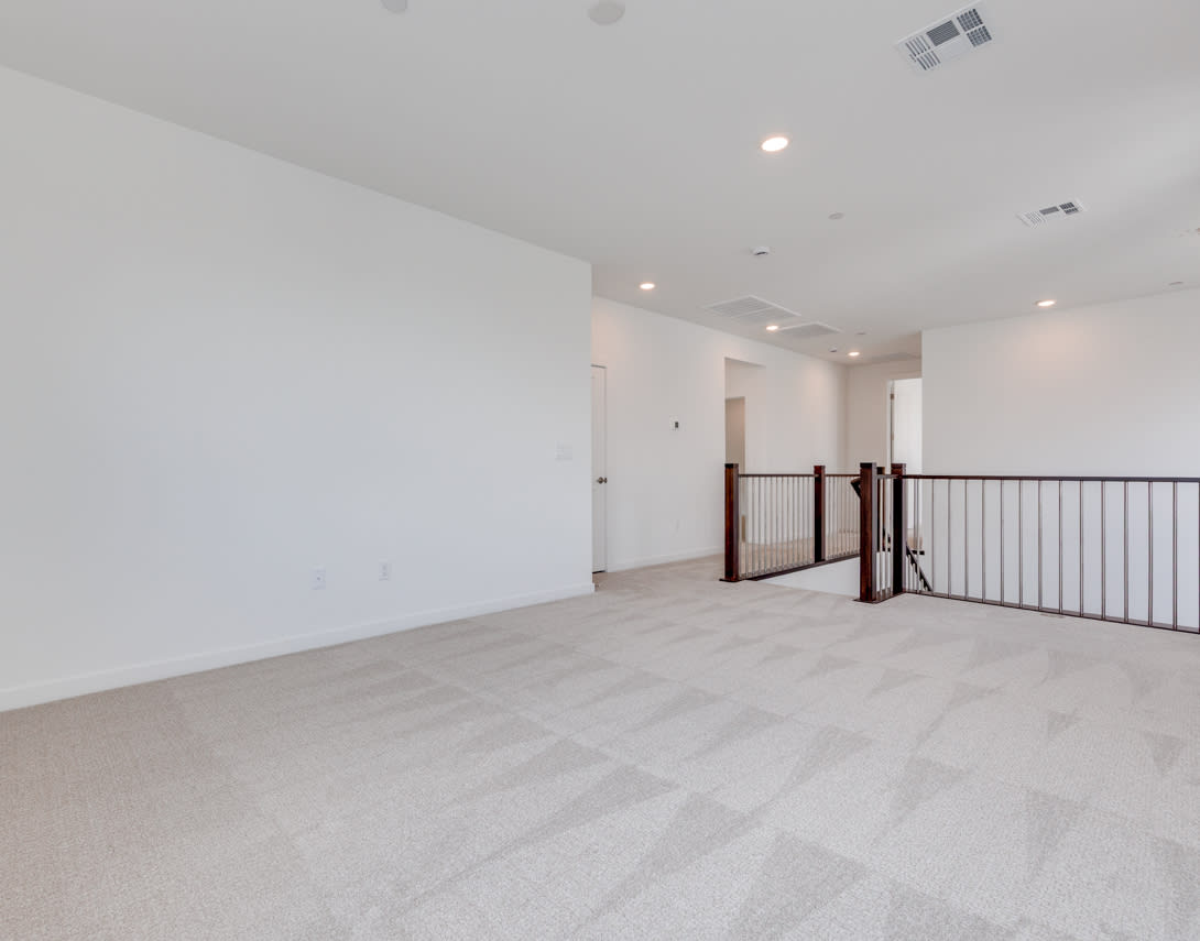 An empty, spacious room with white walls, a wooden railing, and a tiled floor, creating a clean and minimalist atmosphere.