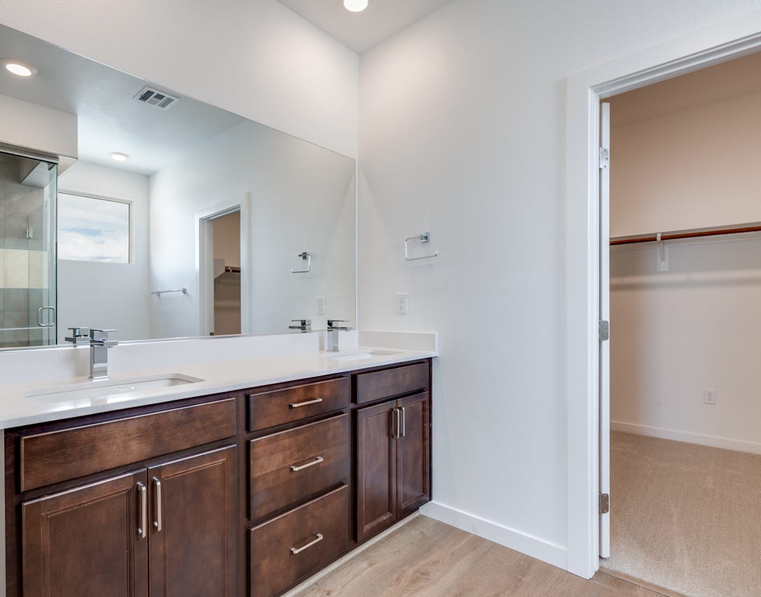 A modern bathroom with a wooden vanity, a large mirror, and a doorway leading to another room.