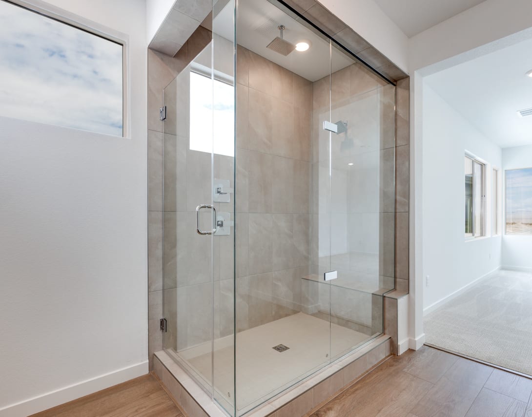 A modern, spacious bathroom with a large glass shower enclosure, tiled walls, and a wooden floor.