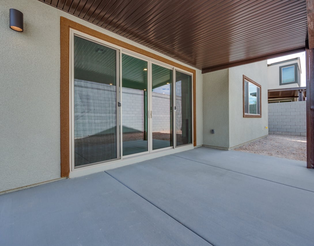 A spacious outdoor patio area with a concrete floor, surrounded by a wooden-paneled wall and large sliding glass doors leading into the interior of the building.