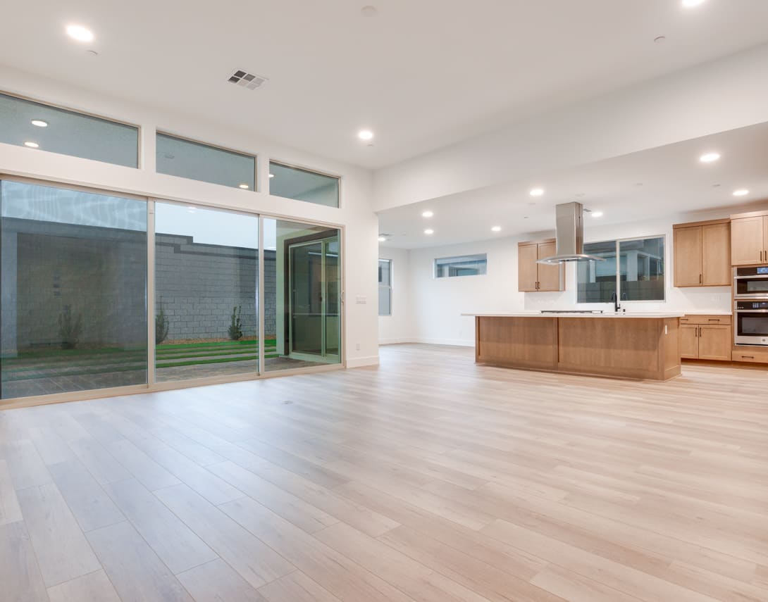 A spacious, modern open-plan living area with a kitchen, hardwood floors, and large sliding glass doors leading to an outdoor space.