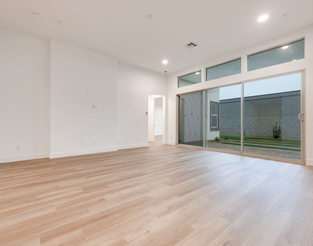 A spacious, minimalist room with a wooden floor, large windows, and a view of a small outdoor area.