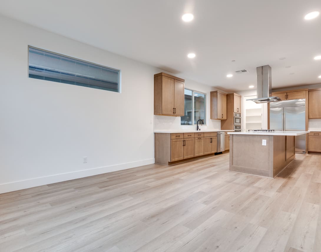 A modern, open-concept kitchen and living space with light-colored wood floors, white walls, and wooden cabinetry.