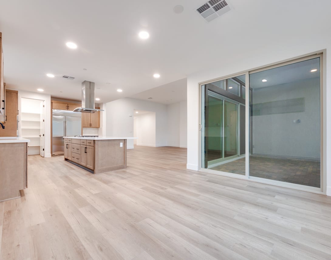 A spacious, modern kitchen with a large sliding glass door leading to an adjacent room, featuring light-colored wood flooring and a central island.