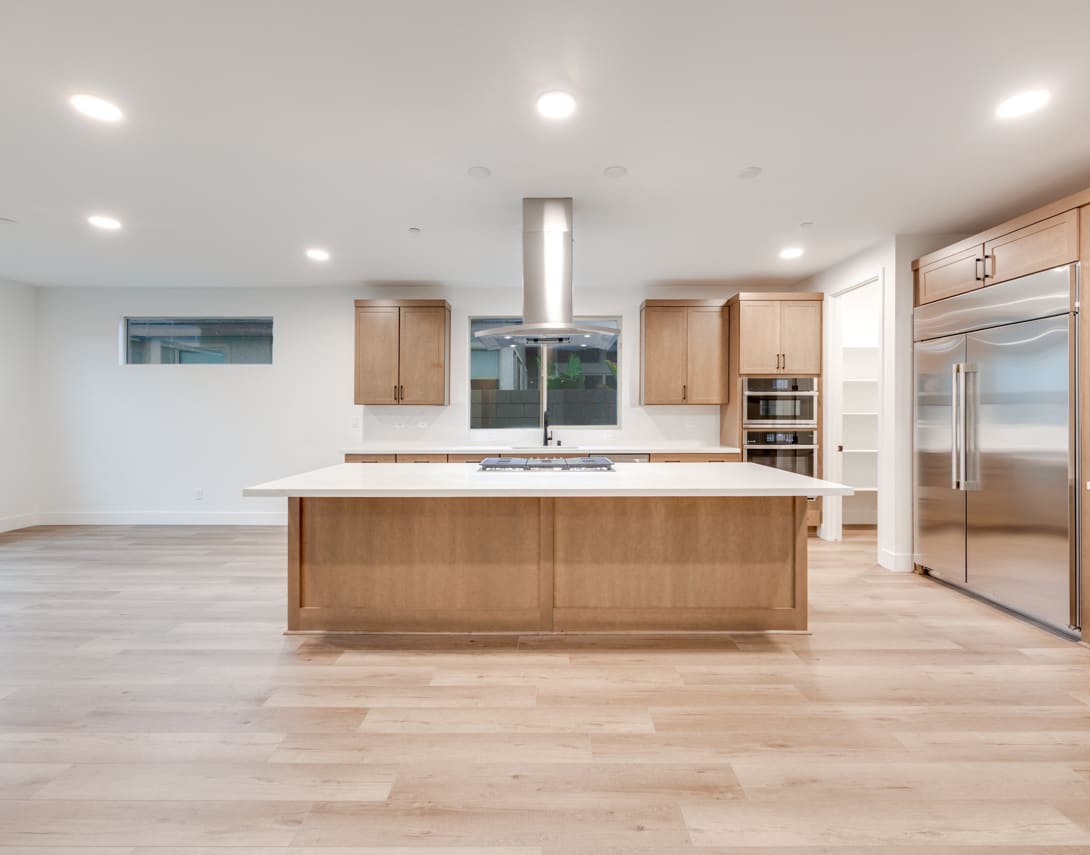 A modern, open-concept kitchen with a large central island, wooden cabinets, and stainless steel appliances, set against a bright and airy backdrop.