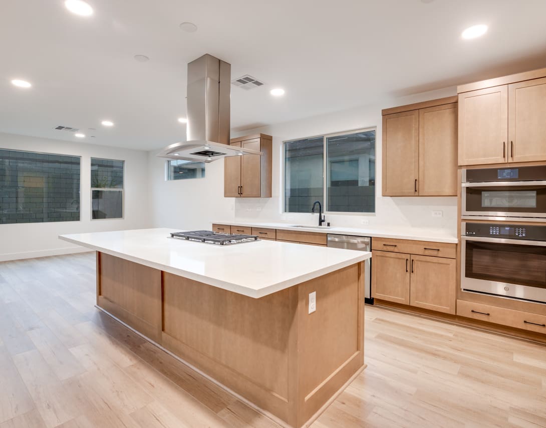 A modern, open-concept kitchen with a large island, light wood cabinets, and stainless steel appliances, set against a backdrop of large windows providing ample natural light.