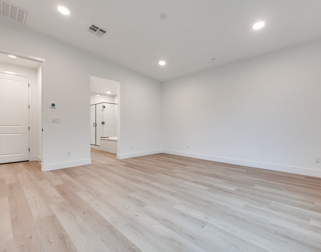 A spacious, well-lit room with white walls and a hardwood floor, featuring a door and a closet in the background.