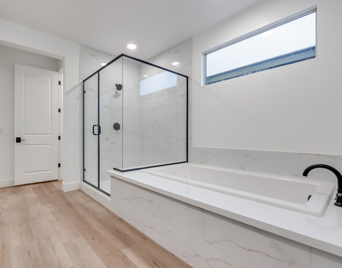 A modern, minimalist bathroom with a large glass-enclosed shower, a freestanding bathtub, and a window providing natural light.