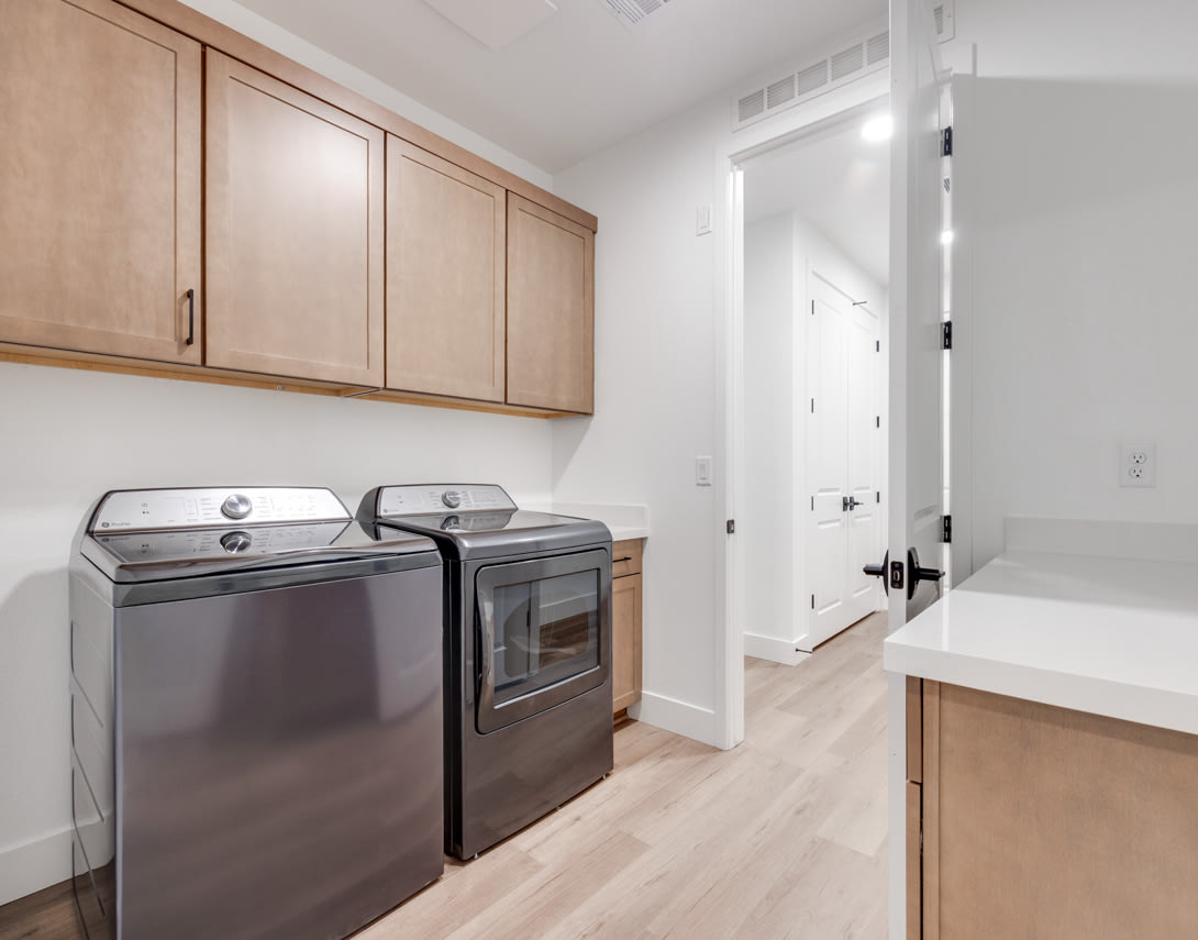 A modern and well-equipped laundry room with stainless steel appliances, wooden cabinets, and a bright, open layout.