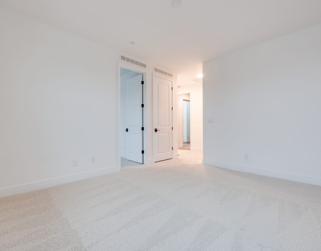 A bright, minimalist room with white walls, a hardwood floor, and two closed doors leading to other areas.