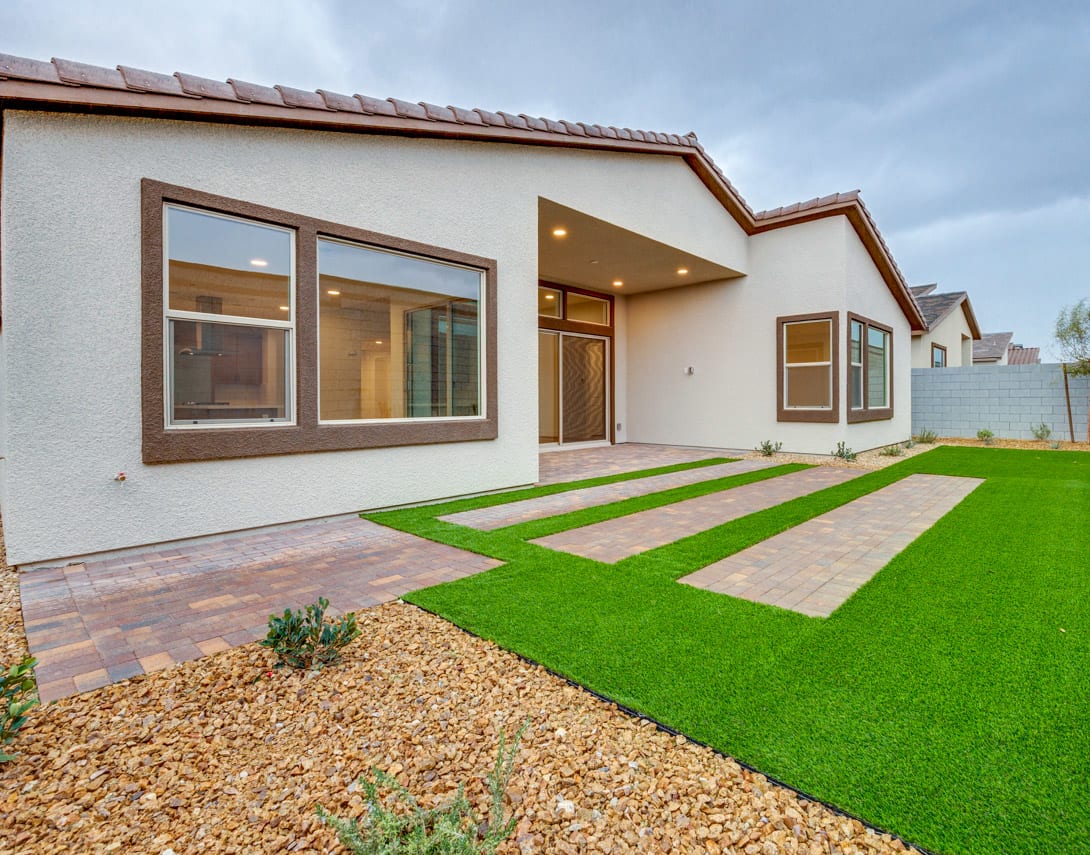 A modern, single-story house with a well-manicured lawn, featuring a paved walkway and landscaping elements in the foreground.