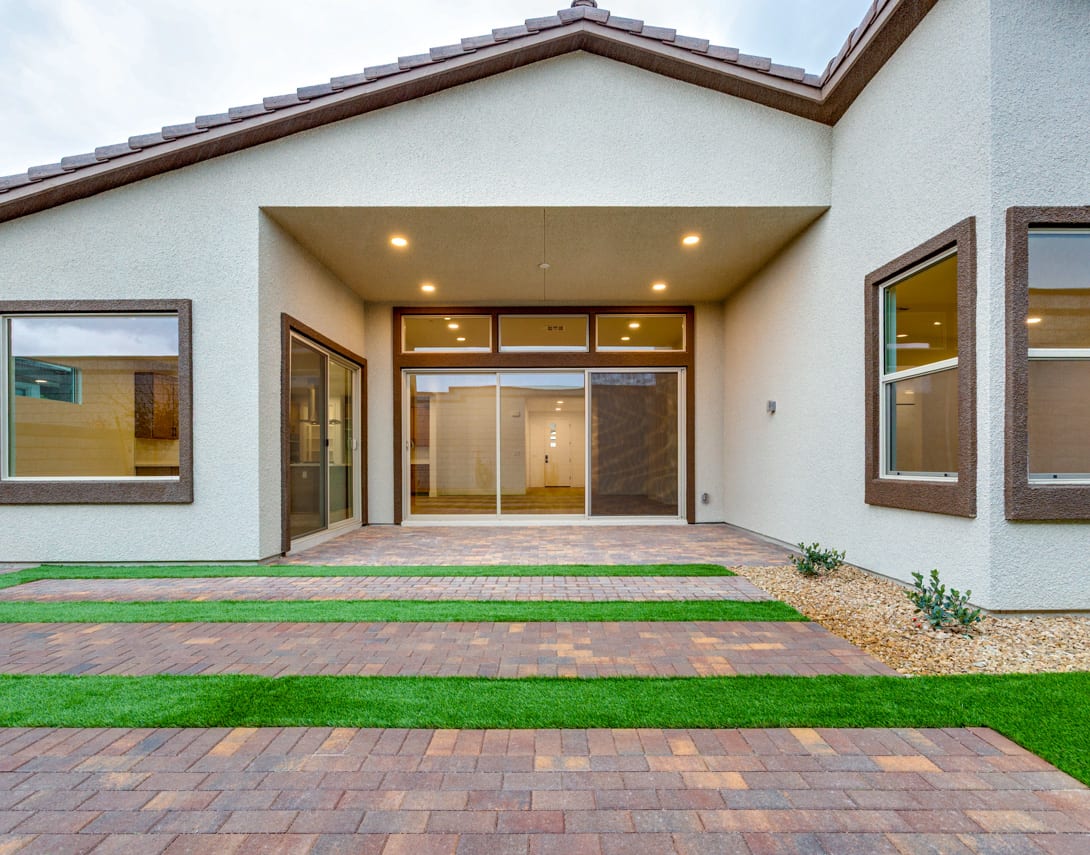 A modern, well-lit residential building with a paved walkway leading to the entrance, surrounded by lush green grass and landscaping.