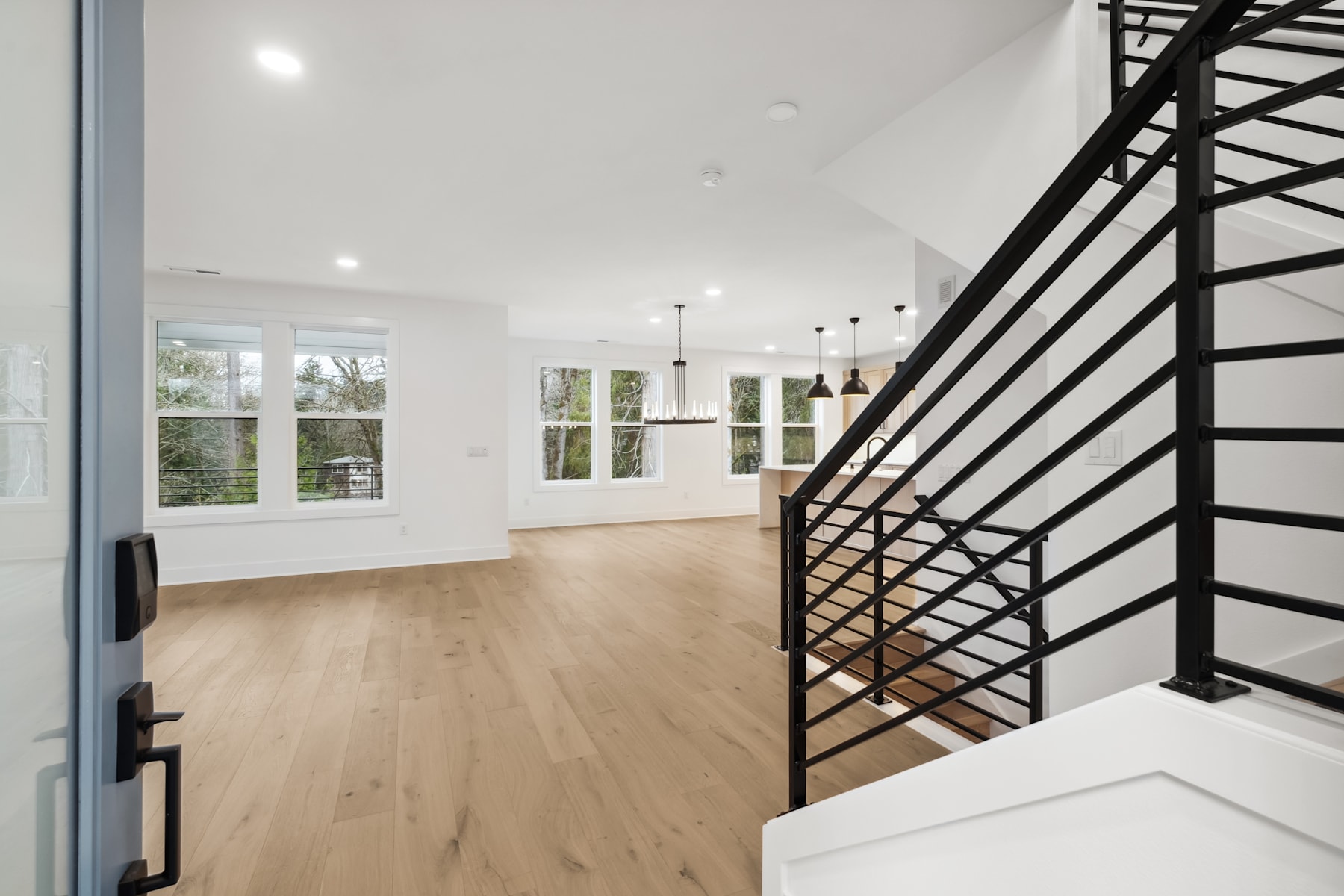 A spacious, modern interior with a wooden floor, large windows, and a black metal staircase leading to an upper level.