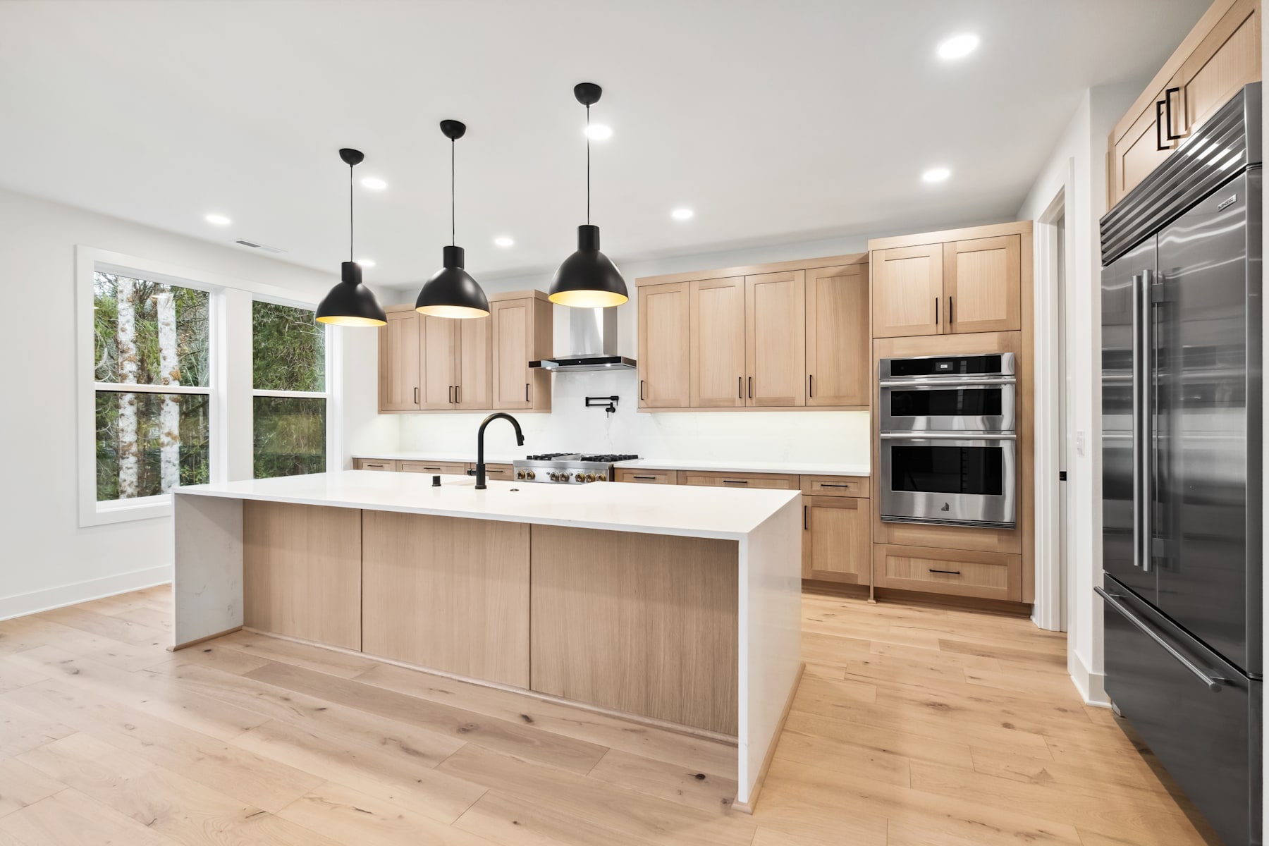 A modern, open-concept kitchen with light wood cabinetry, a central island, and pendant lighting fixtures hanging above.