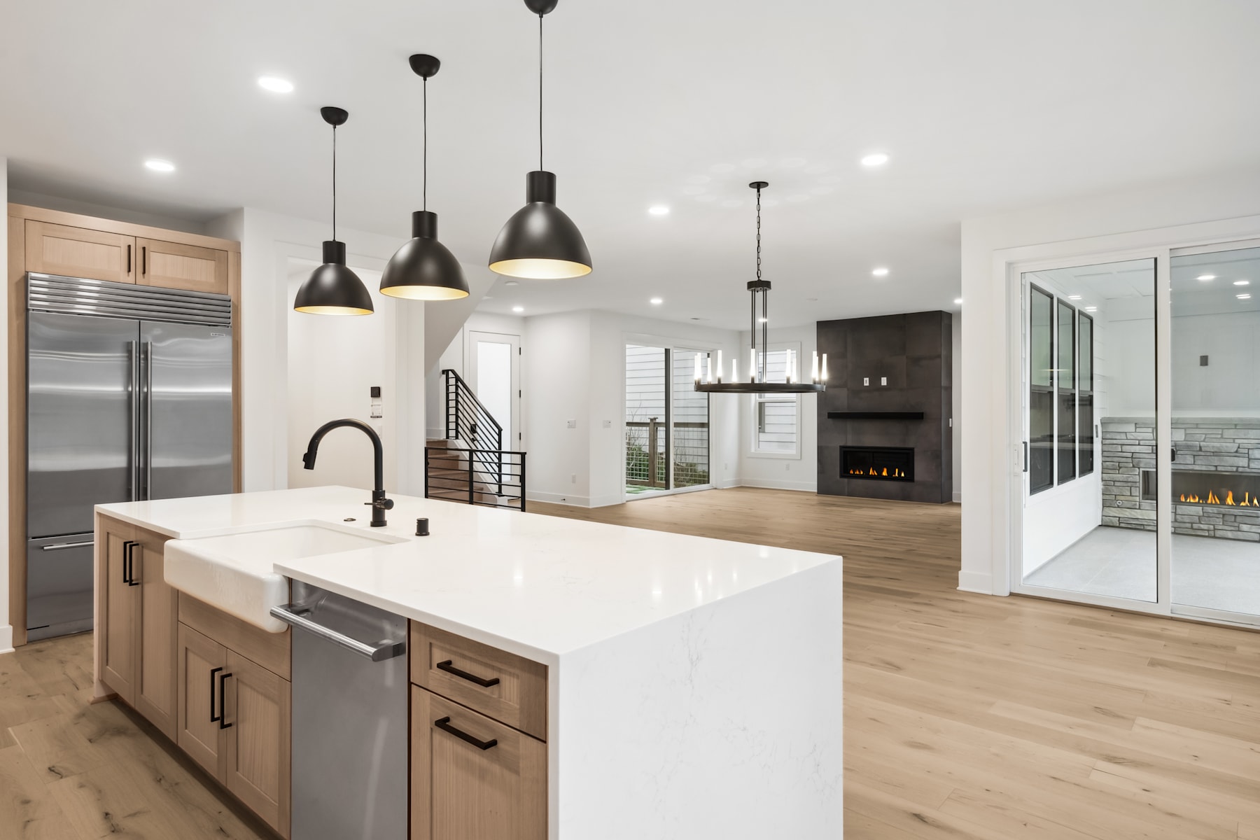A modern, open-concept kitchen with a large island, pendant lighting, and a fireplace visible in the background.