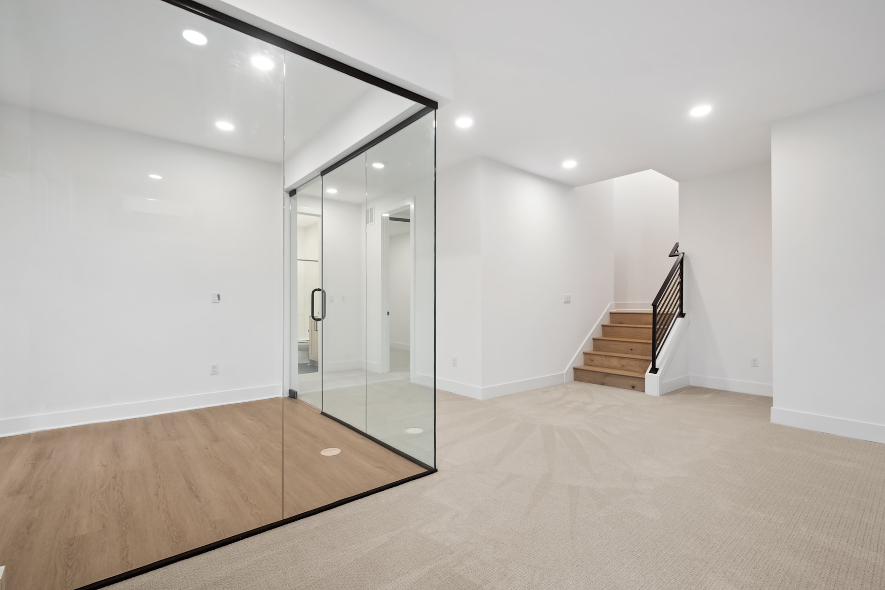 A spacious, minimalist entryway with a large glass door, wooden flooring, and a staircase leading to the upper level.