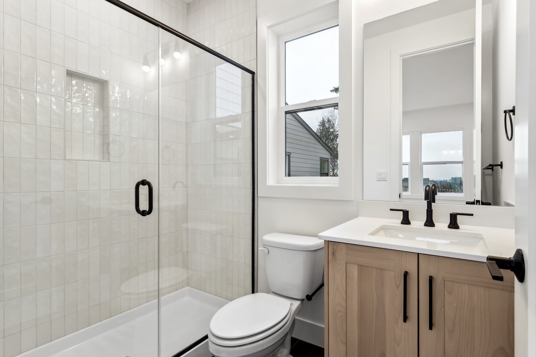 A modern, minimalist bathroom with a glass-enclosed shower, a white vanity with a sink, and a window providing natural light.