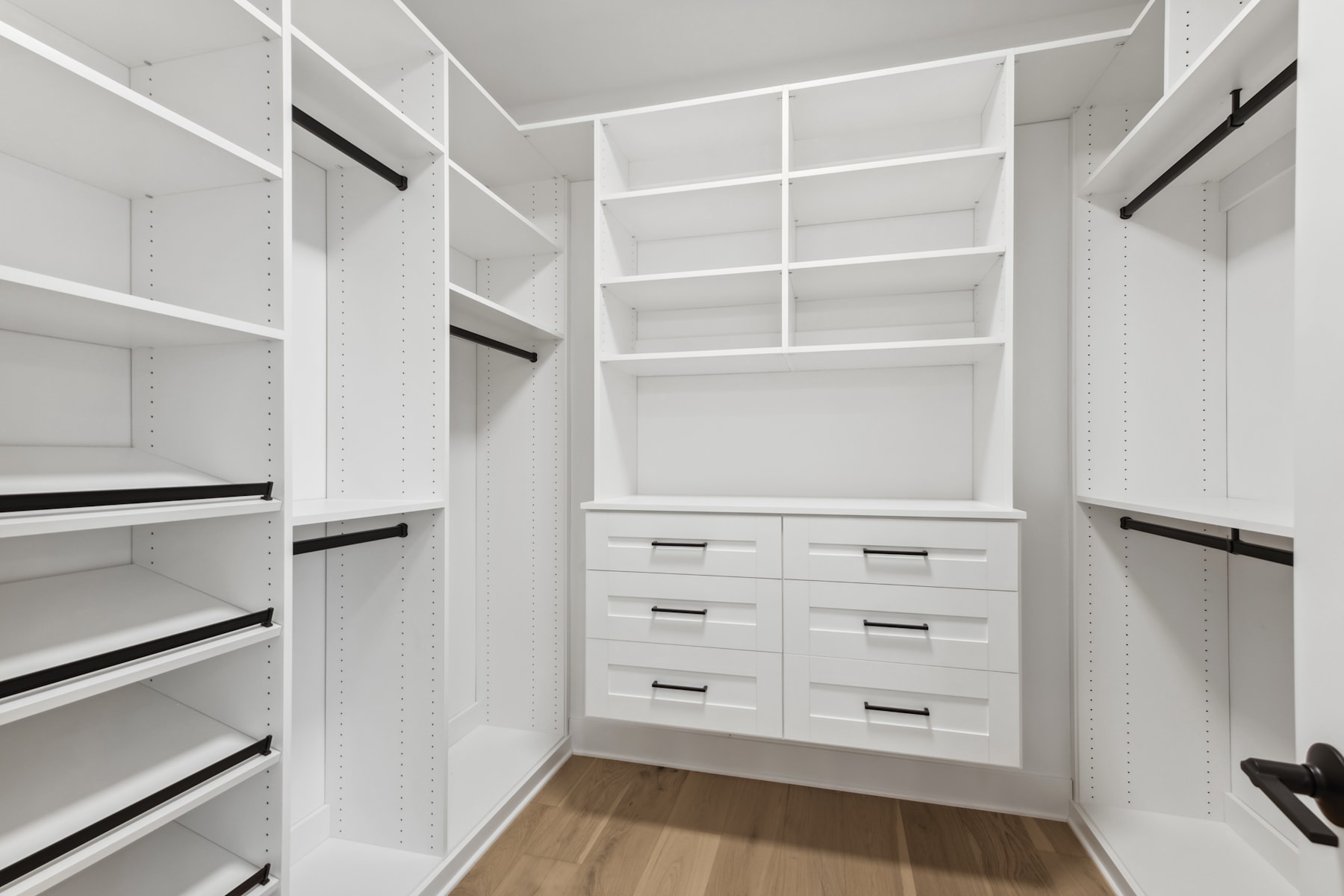 A spacious and well-organized walk-in closet with white shelves, drawers, and a wooden floor.