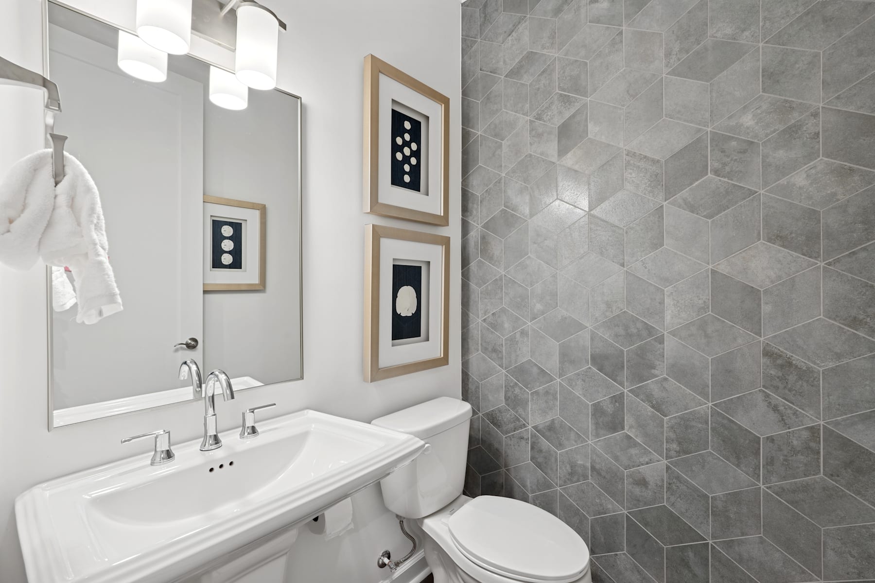 A modern and minimalist bathroom with a white sink, framed artwork on the walls, and a tiled wall in shades of gray.