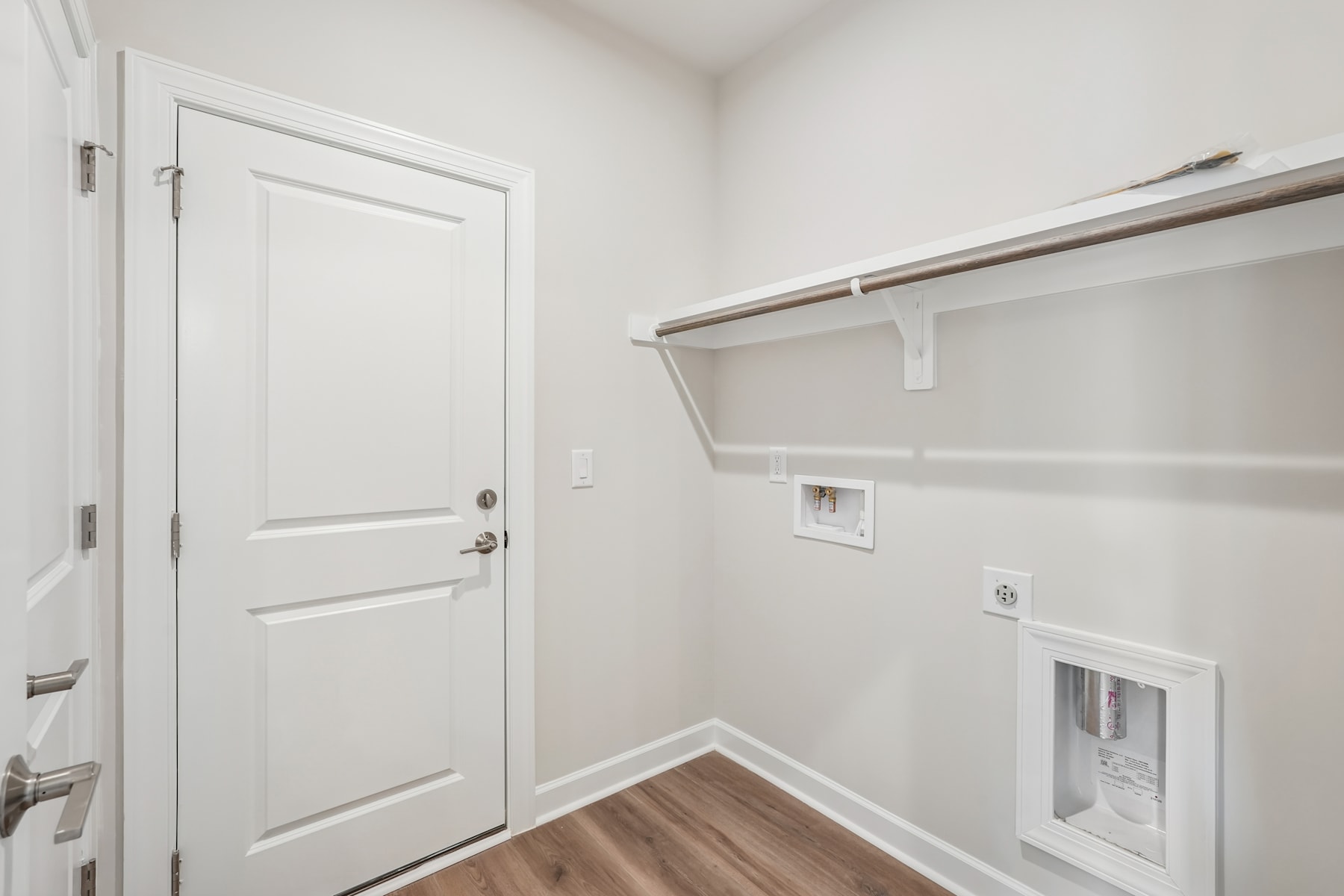 A white door in the foreground leads into a small, minimalist room with a closet and shelving unit visible in the background.