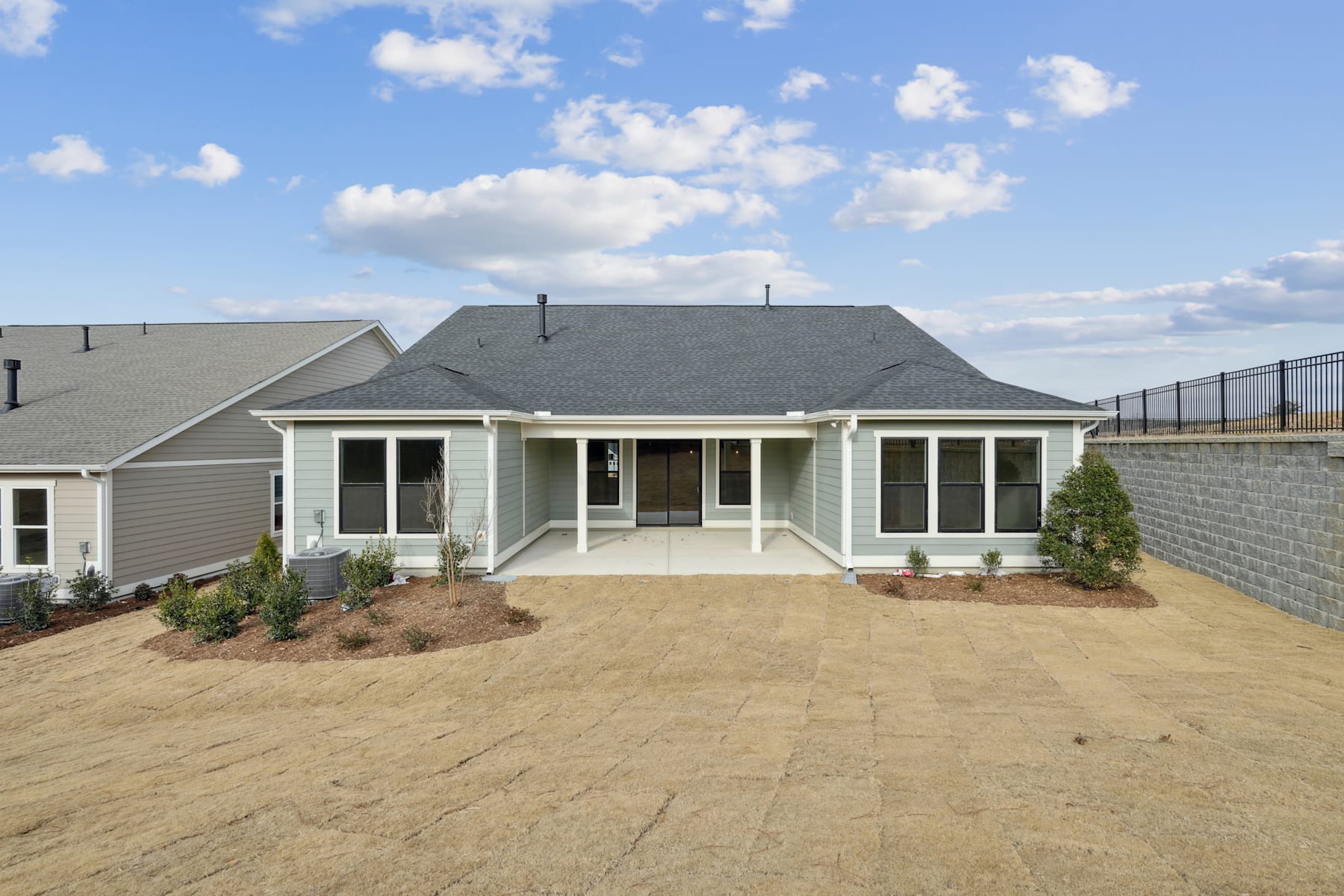 A single-story house with a porch and a landscaped yard in the foreground, set against a blue sky with scattered clouds in the background.