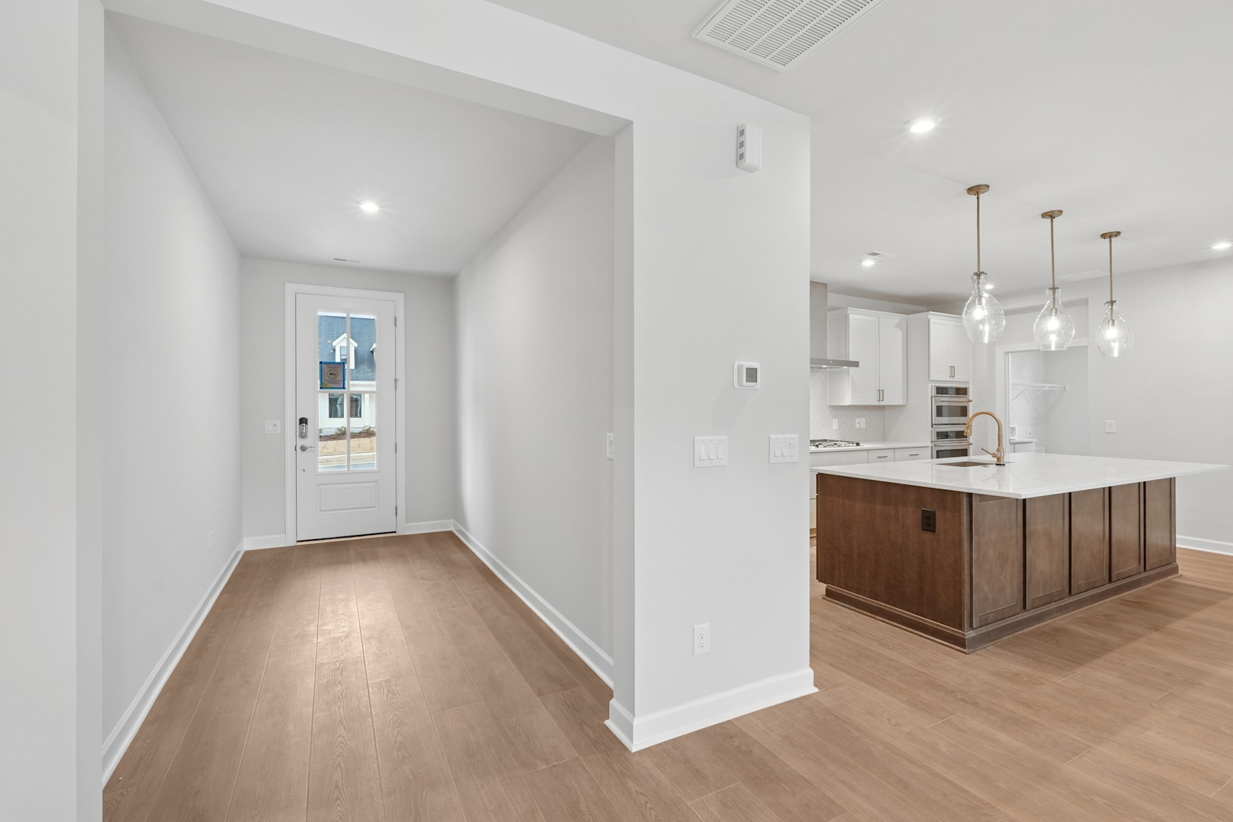 A bright, modern entryway leads into a spacious kitchen with a wooden island and sleek white cabinetry.