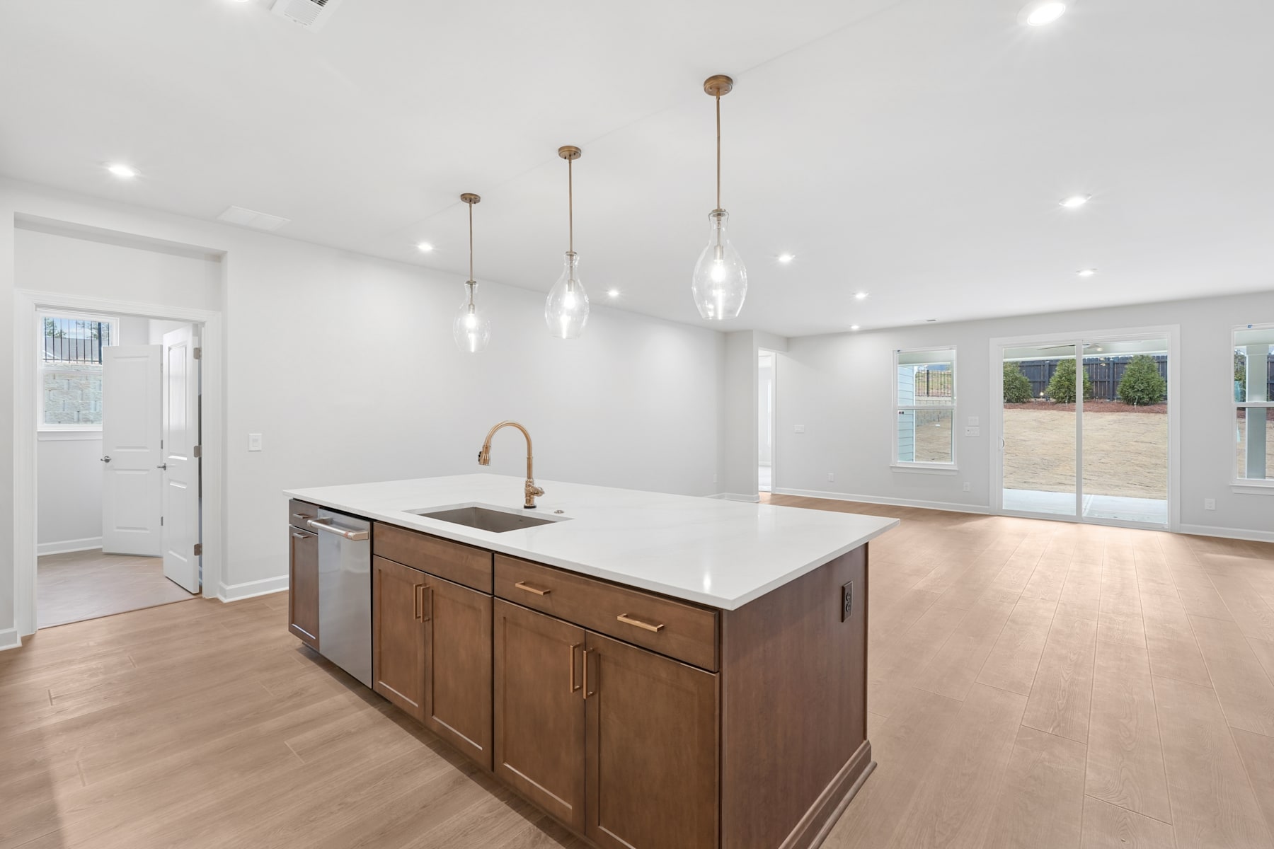 A modern, open-concept kitchen with a large island, wooden cabinets, and pendant lighting fixtures, set against a bright and airy background.