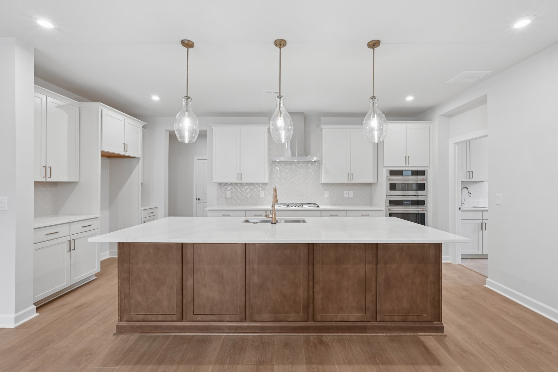 A modern, open-concept kitchen with white cabinets, a large wooden island, and pendant lights hanging above.