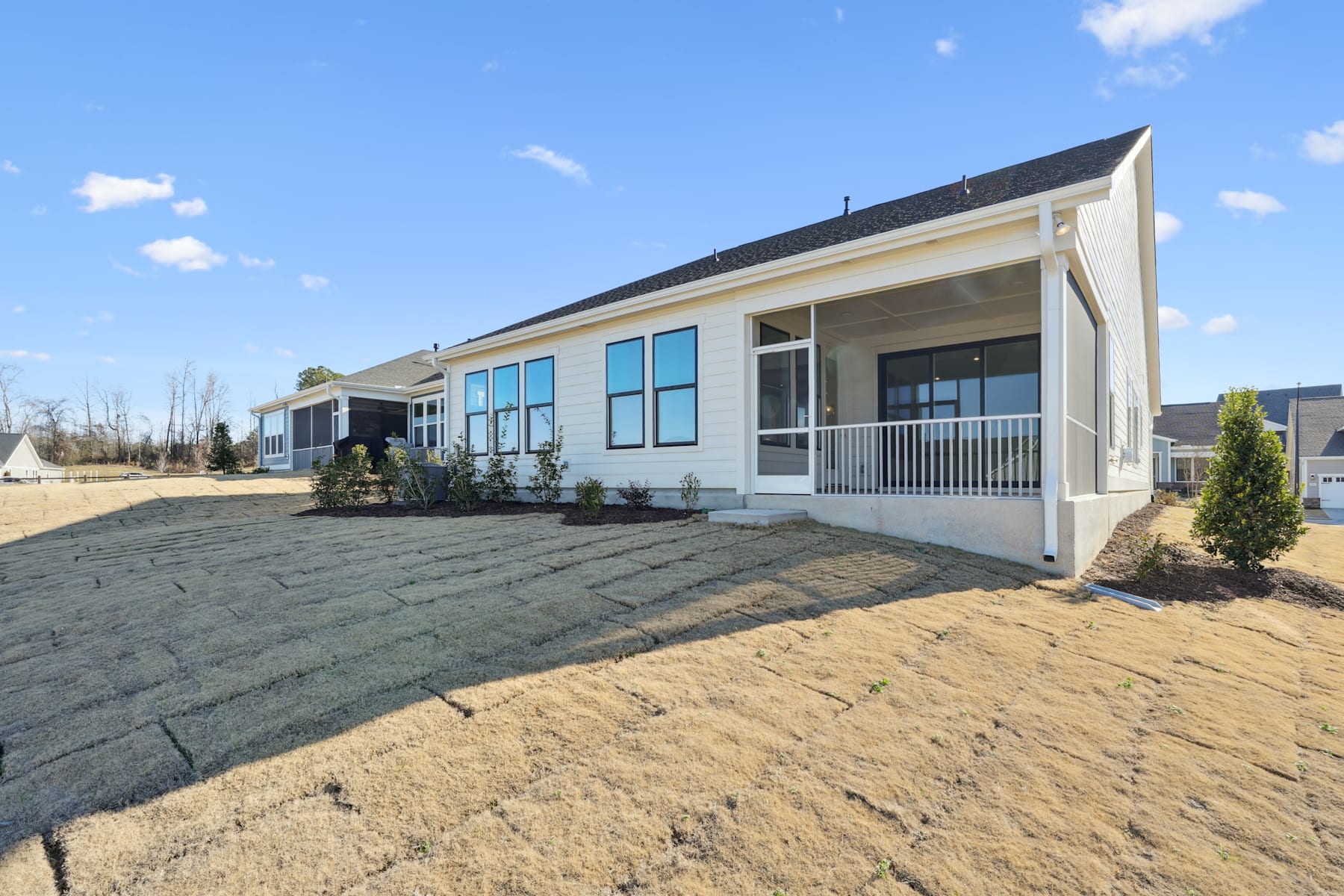 A modern, single-story house with a porch and large windows, surrounded by a freshly landscaped yard with a grassy area in the foreground.