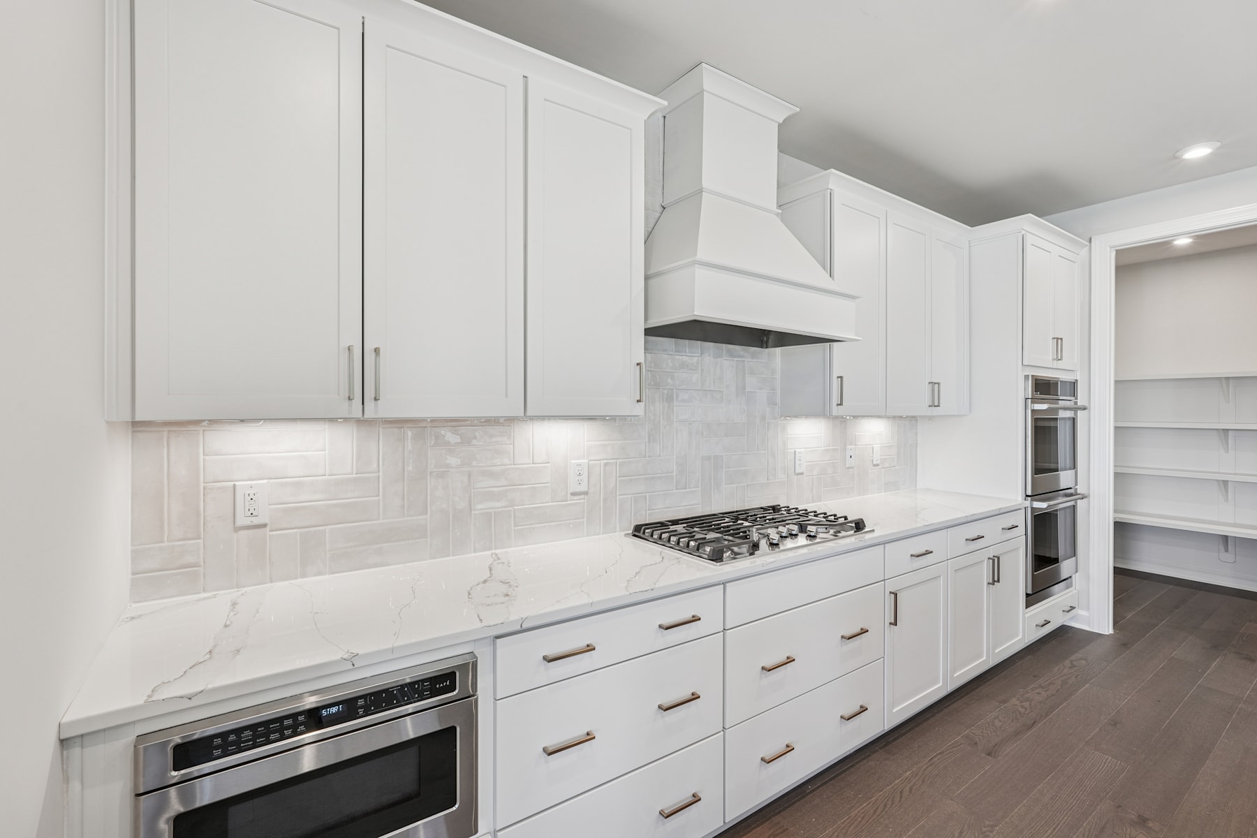 A modern, minimalist kitchen with white cabinets, a marble backsplash, and stainless steel appliances.