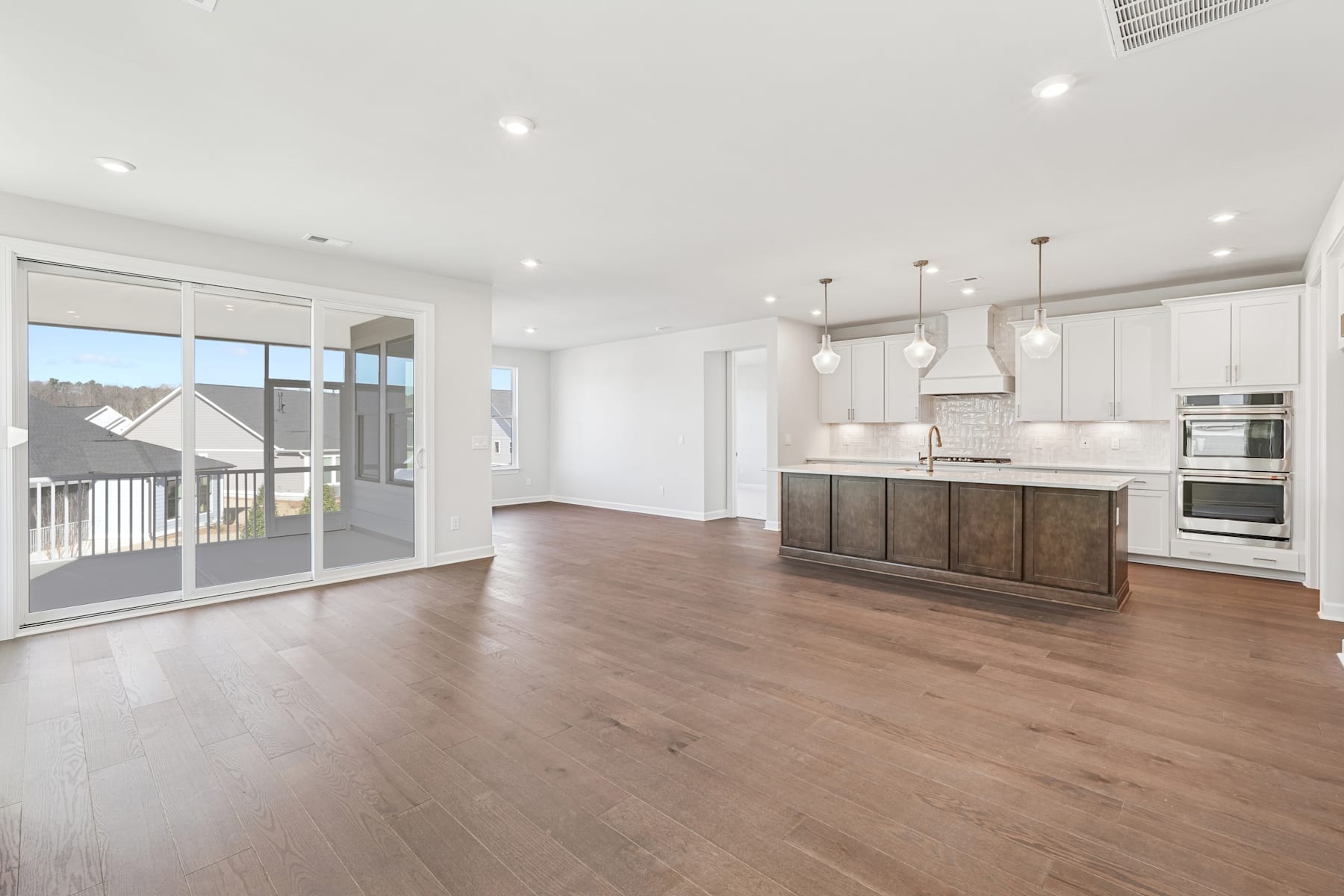 A spacious and modern kitchen with white cabinets, wooden floors, and large windows overlooking a balcony or patio area.