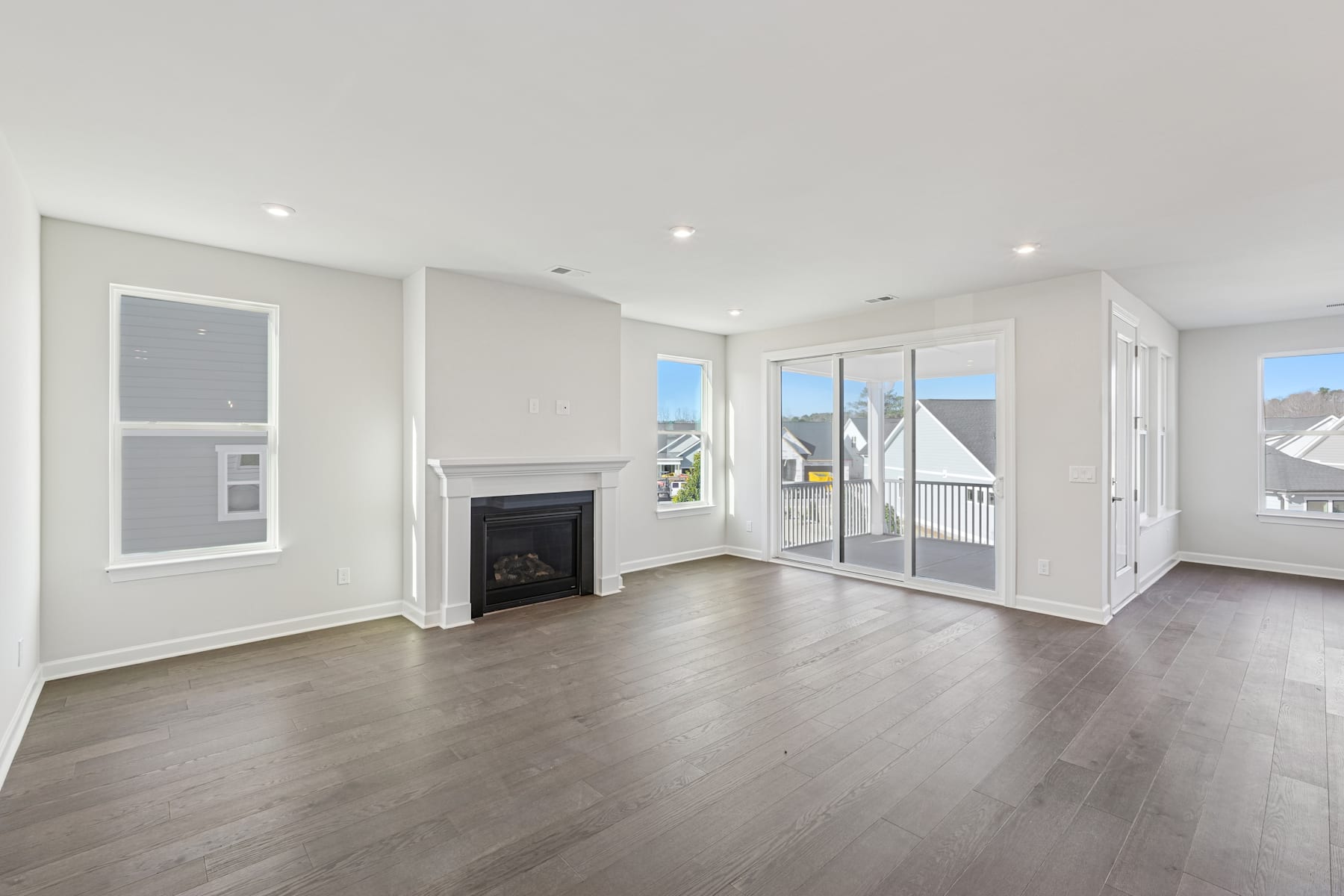 A spacious and bright living room with a fireplace, large windows, and hardwood floors. The room has a modern and minimalist design with a neutral color palette.