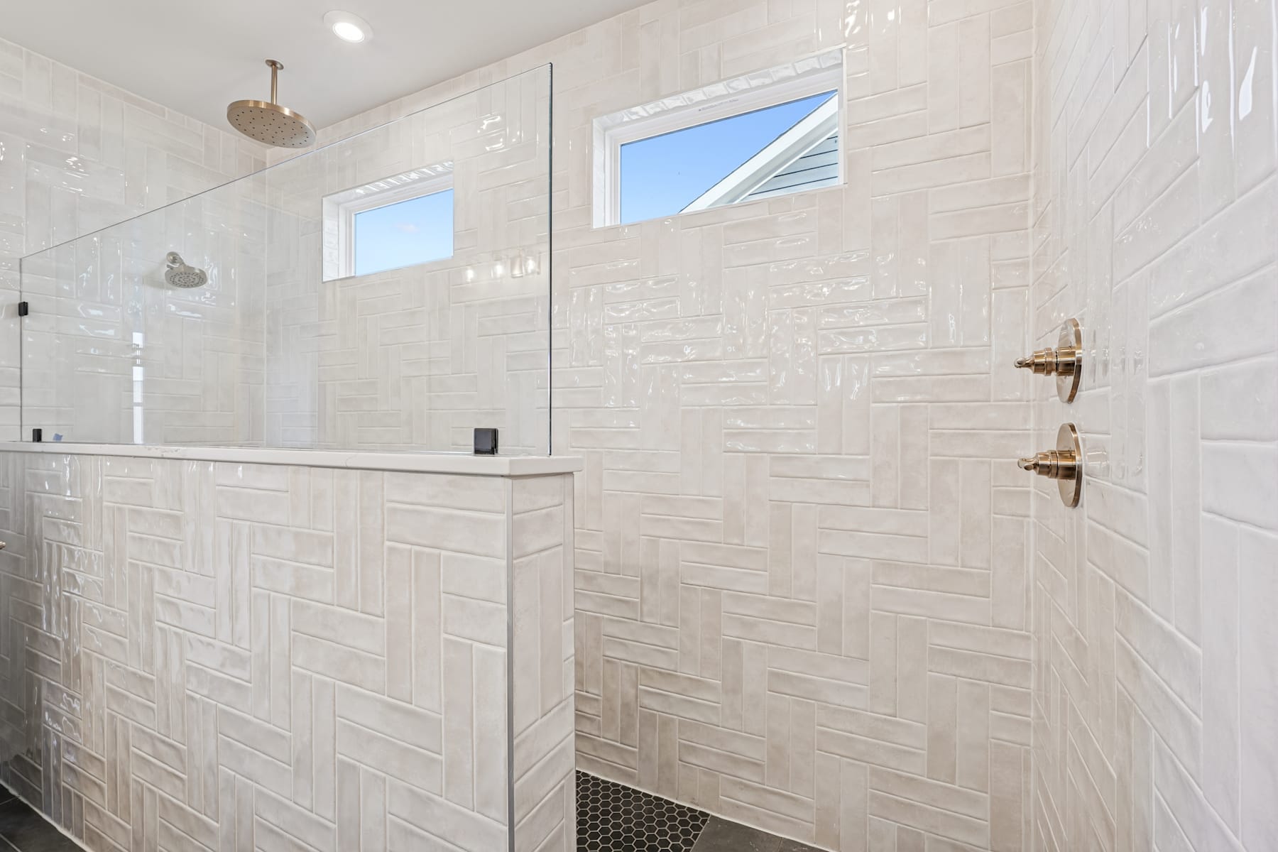 A modern, minimalist bathroom with white tile walls, a glass shower enclosure, and a window providing natural light.
