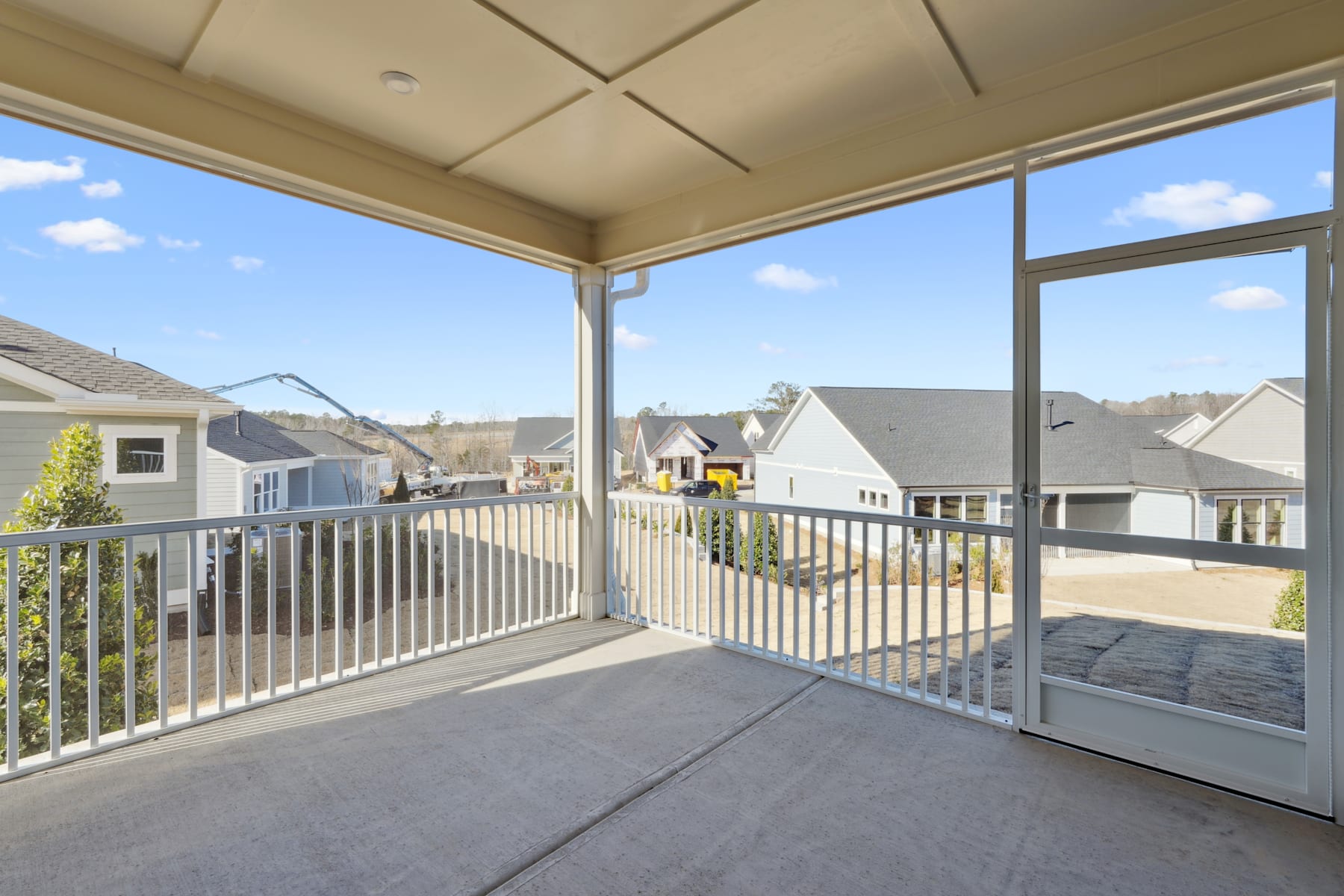 A covered patio or balcony overlooking a residential neighborhood, with a clear blue sky and scattered clouds visible through the windows.