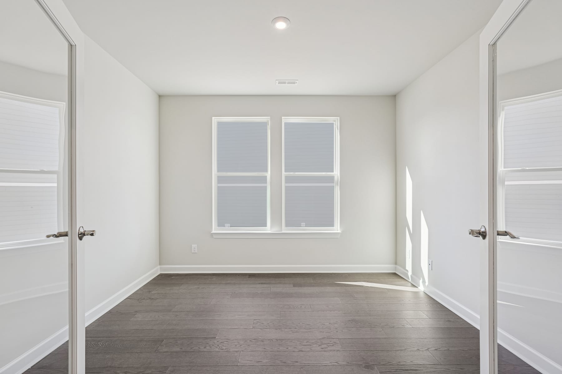 A bright, minimalist room with white walls, a hardwood floor, and a window providing natural light.