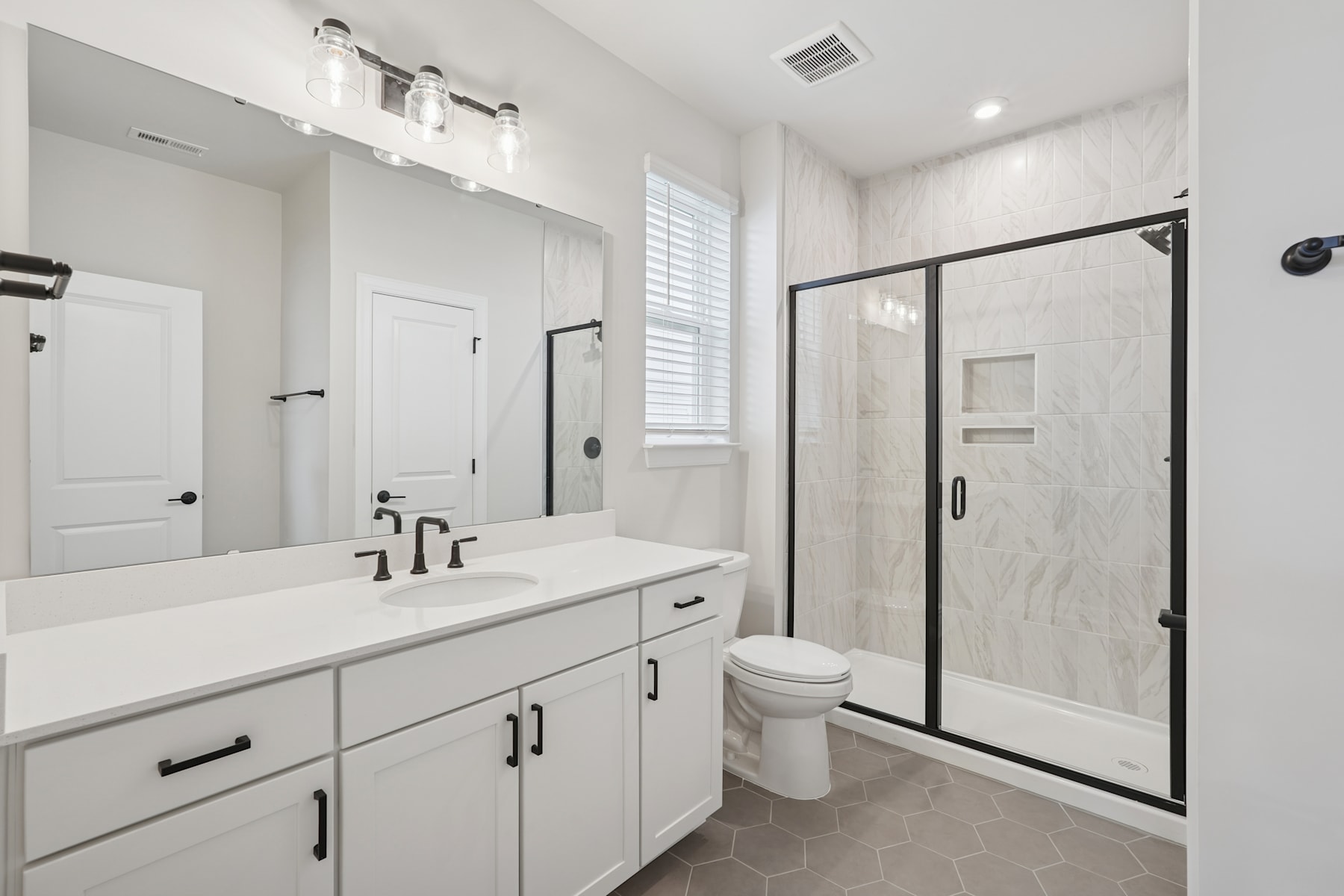A modern, minimalist bathroom with a white vanity, black framed shower enclosure, and hexagonal tile flooring.