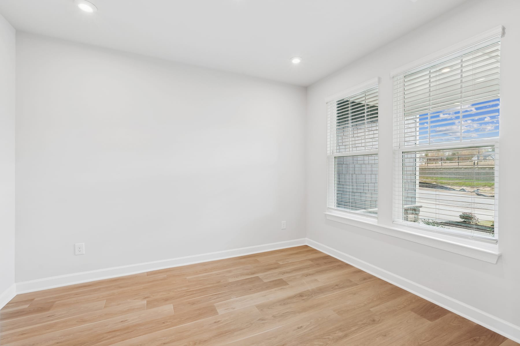 A bright, empty room with white walls, a large window, and hardwood flooring.